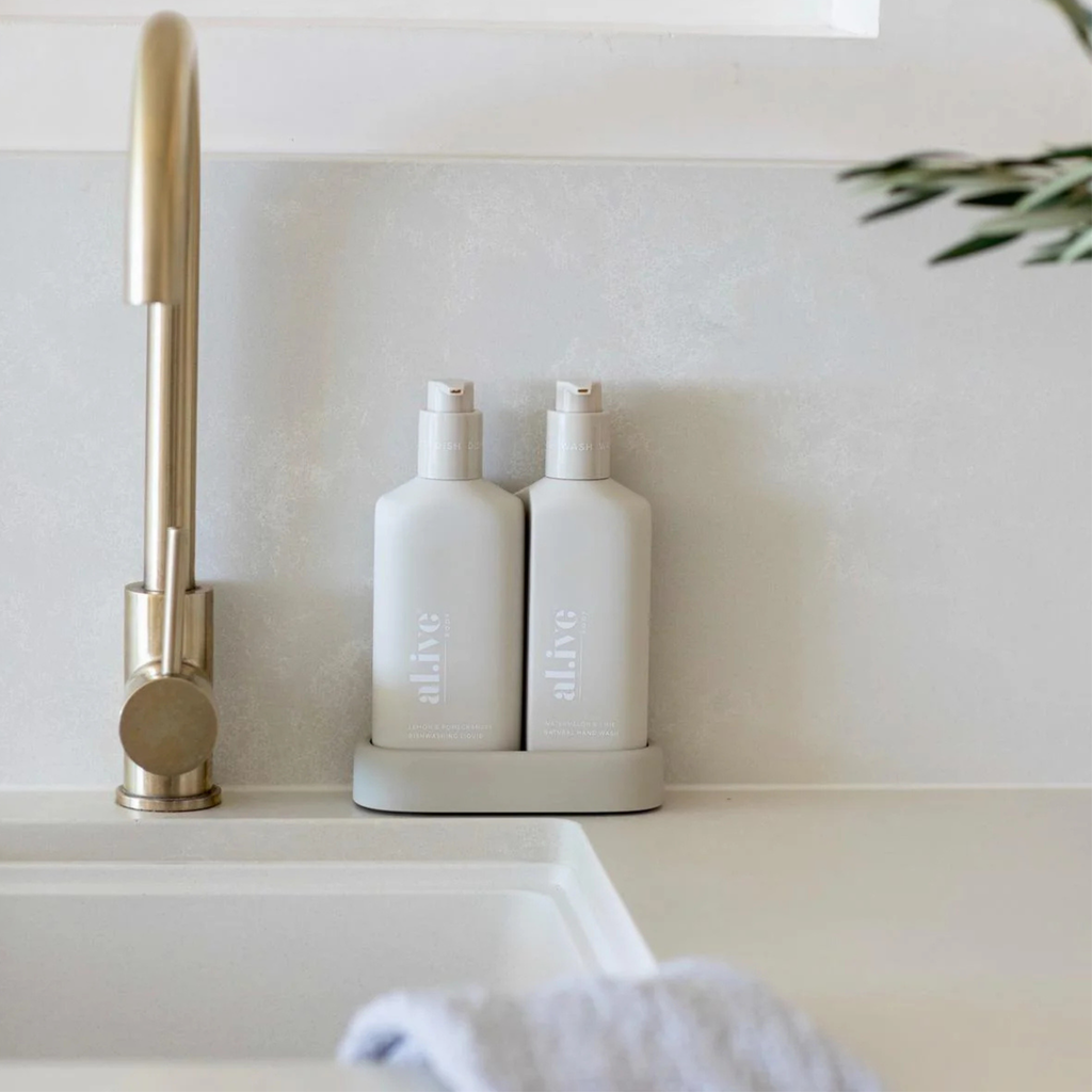 Two white bottles labeled 'alive' on a kitchen counter next to a gold faucet.