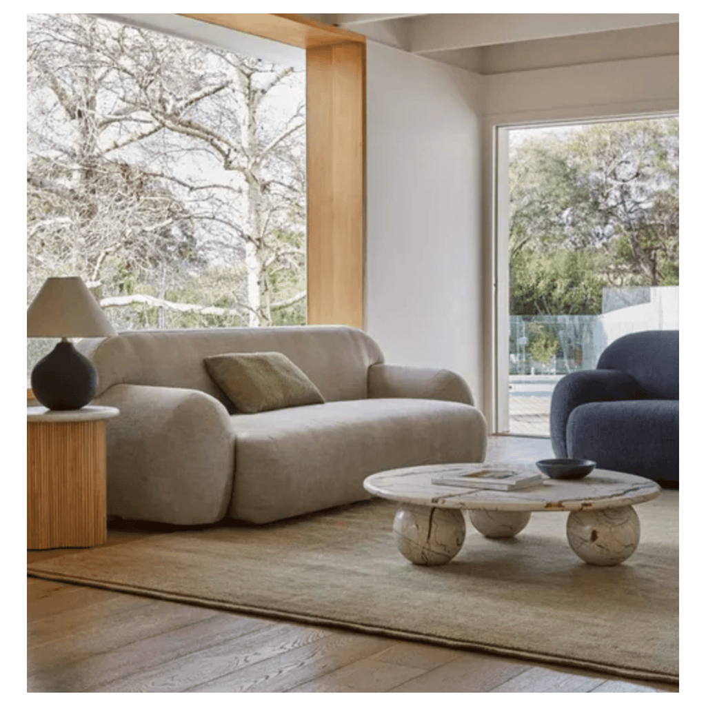 Modern living room with a beige and blue  sofa, marble coffee table, and large windows.