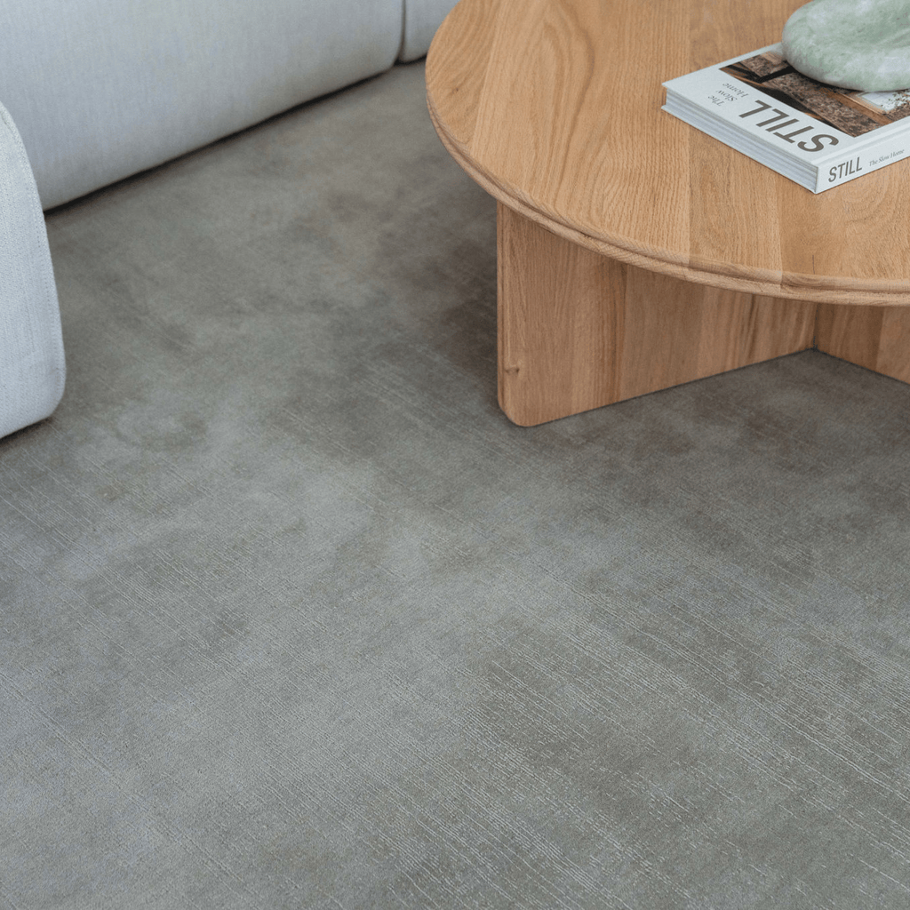 Gray green sage textured floor with a wooden coffee table and magazine in a living room setting.