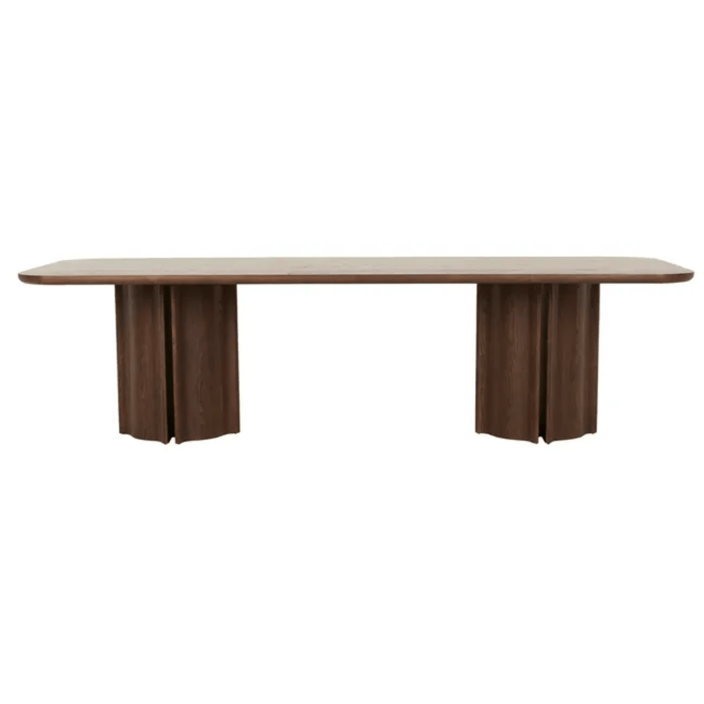 Dark ash wood Leon dining table with softly curved top corners, supported by bold, vertically fluted legs in tobacco finish.
