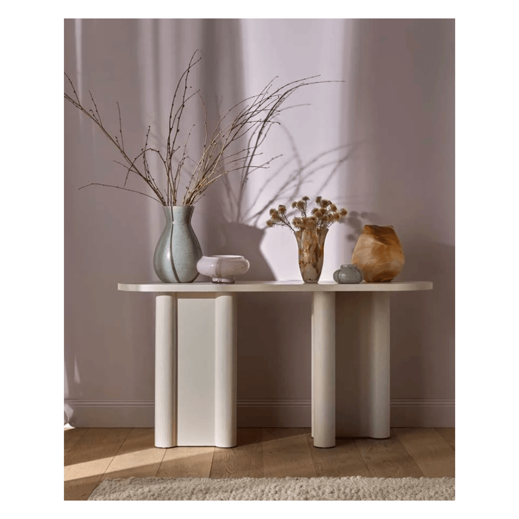 Modern oval hall table with decorative vases and plants against a plain wall