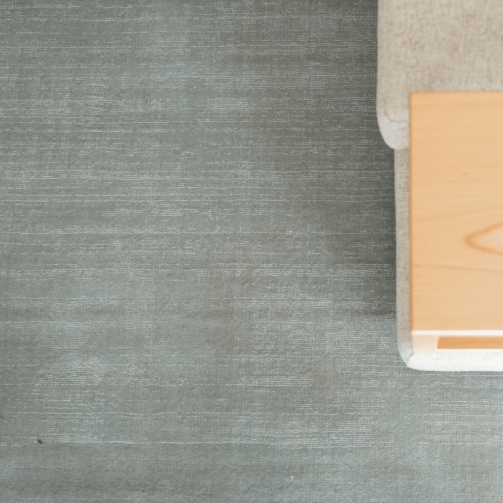 sage green textured surface with a corner of a beige sofa and wooden table.