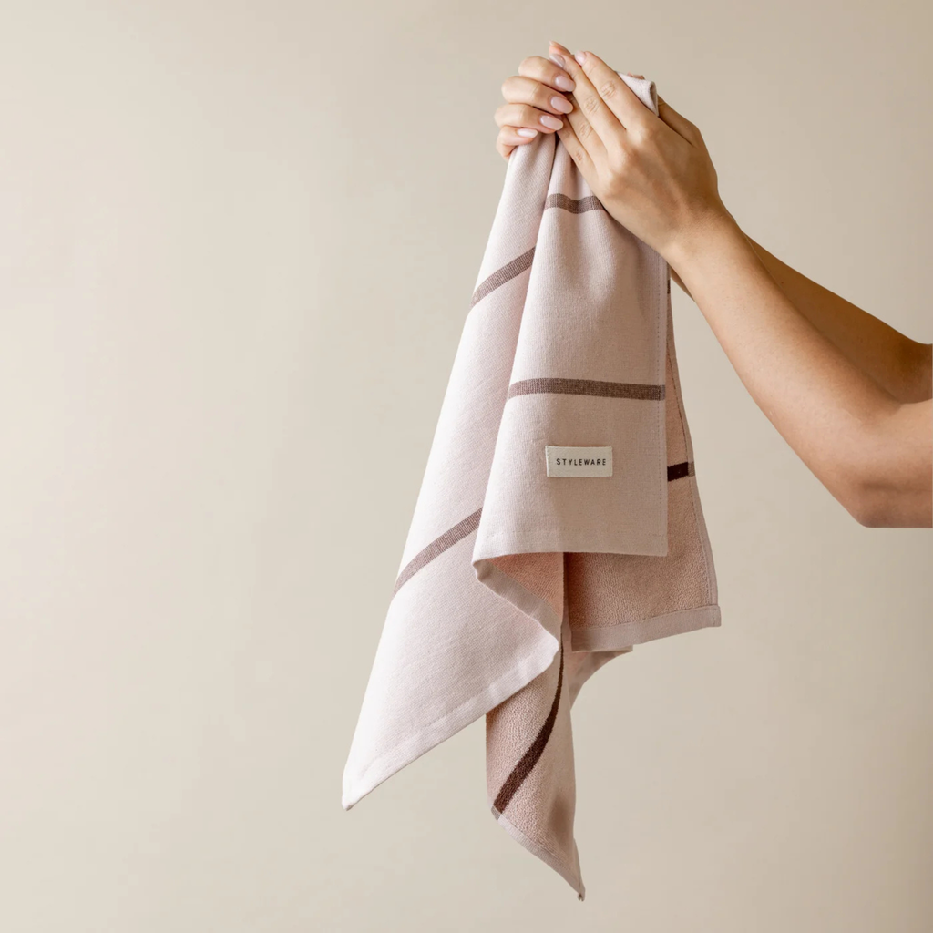 Person holding a pink towel with a brand label against a beige background